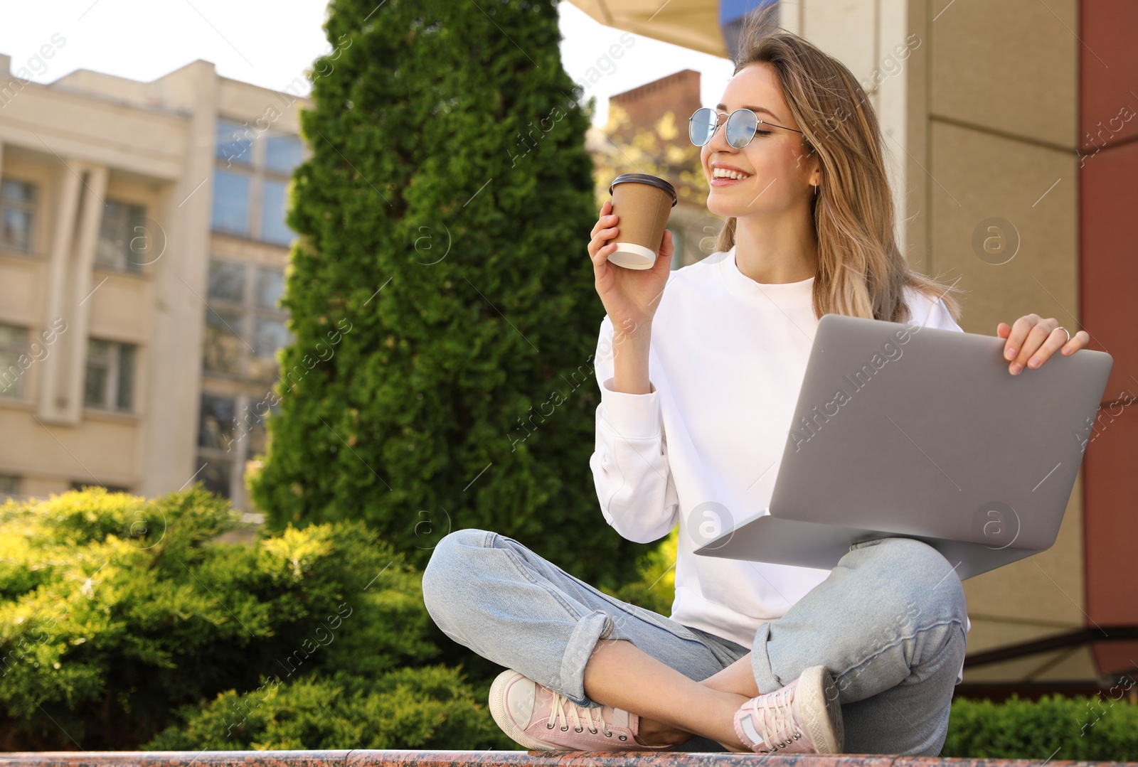 Image of Young woman with paper cup of coffee working on laptop outdoors