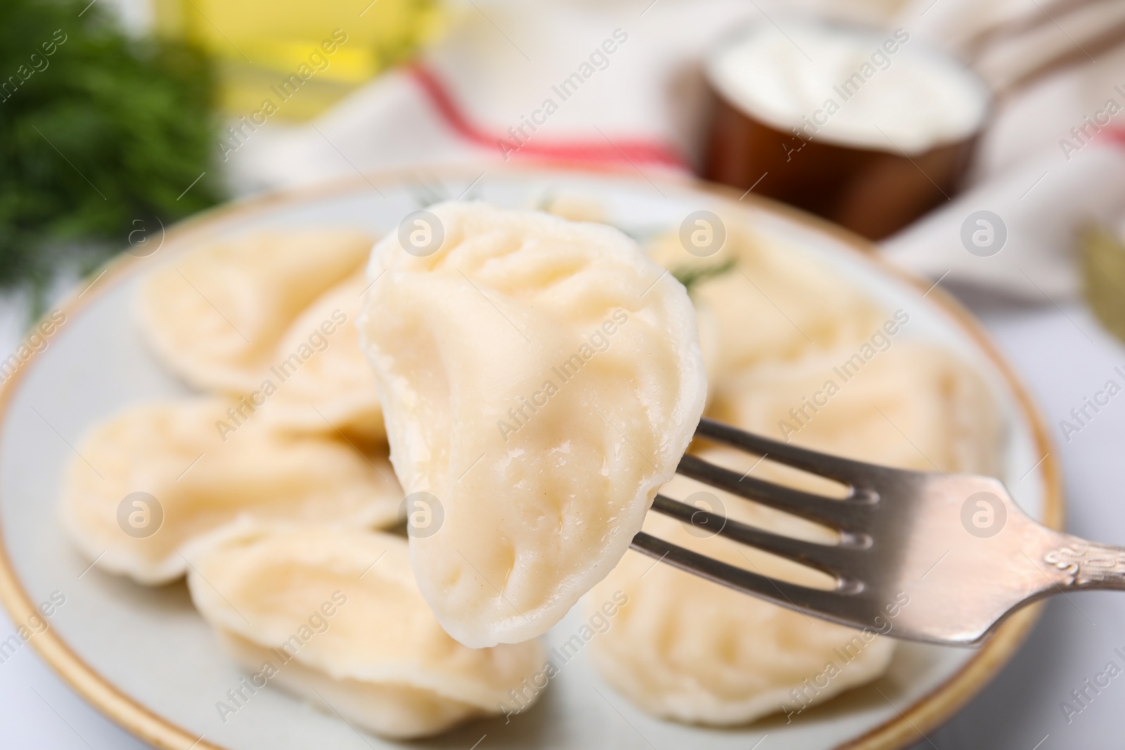 Photo of Fork with delicious dumpling (varenyk) over plate, closeup view