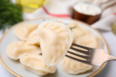Fork with delicious dumpling (varenyk) over plate, closeup view