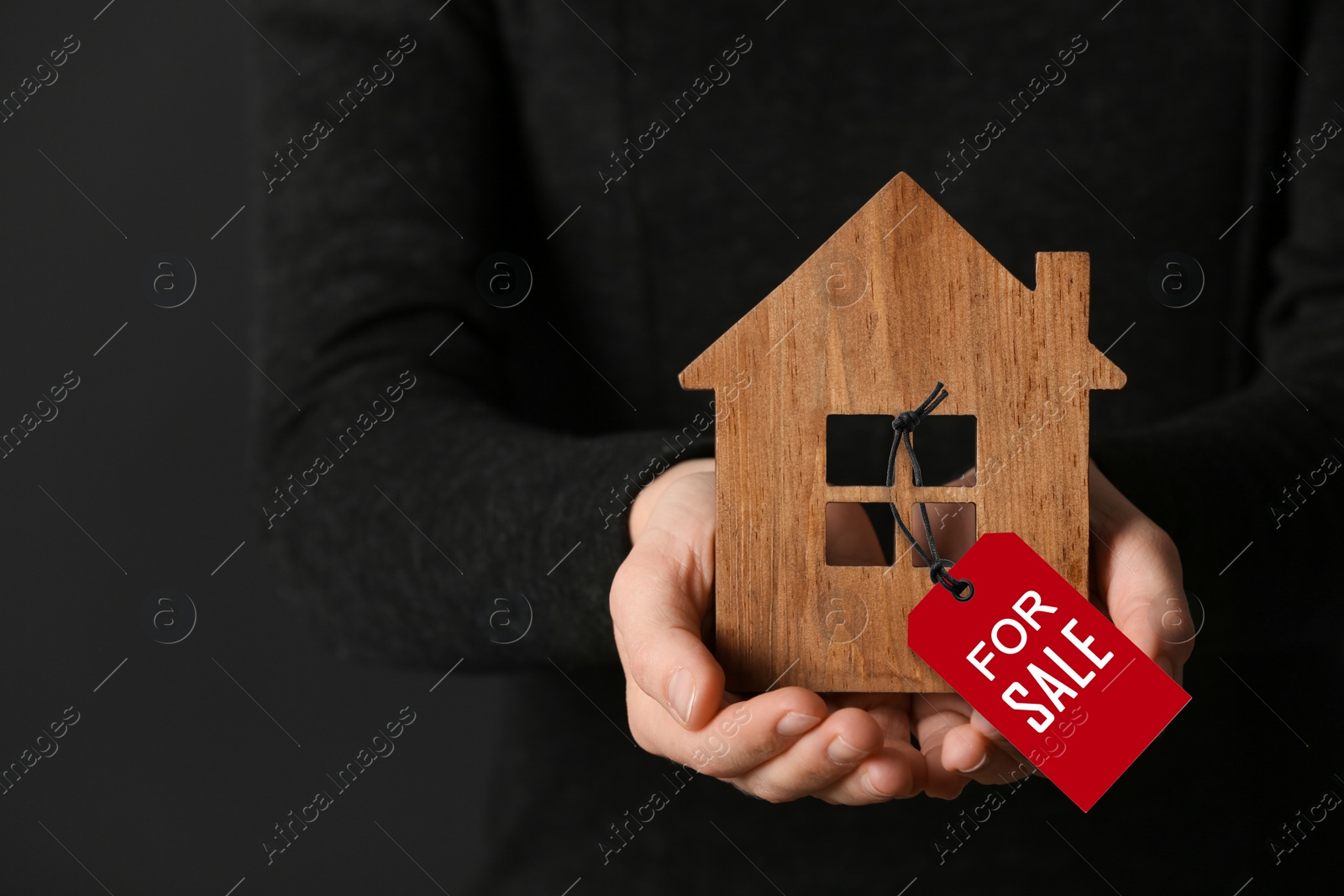 Image of Woman holding wooden house with SALE label on dark background, closeup