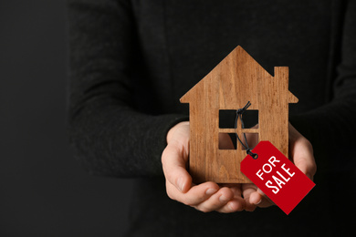 Image of Woman holding wooden house with SALE label on dark background, closeup