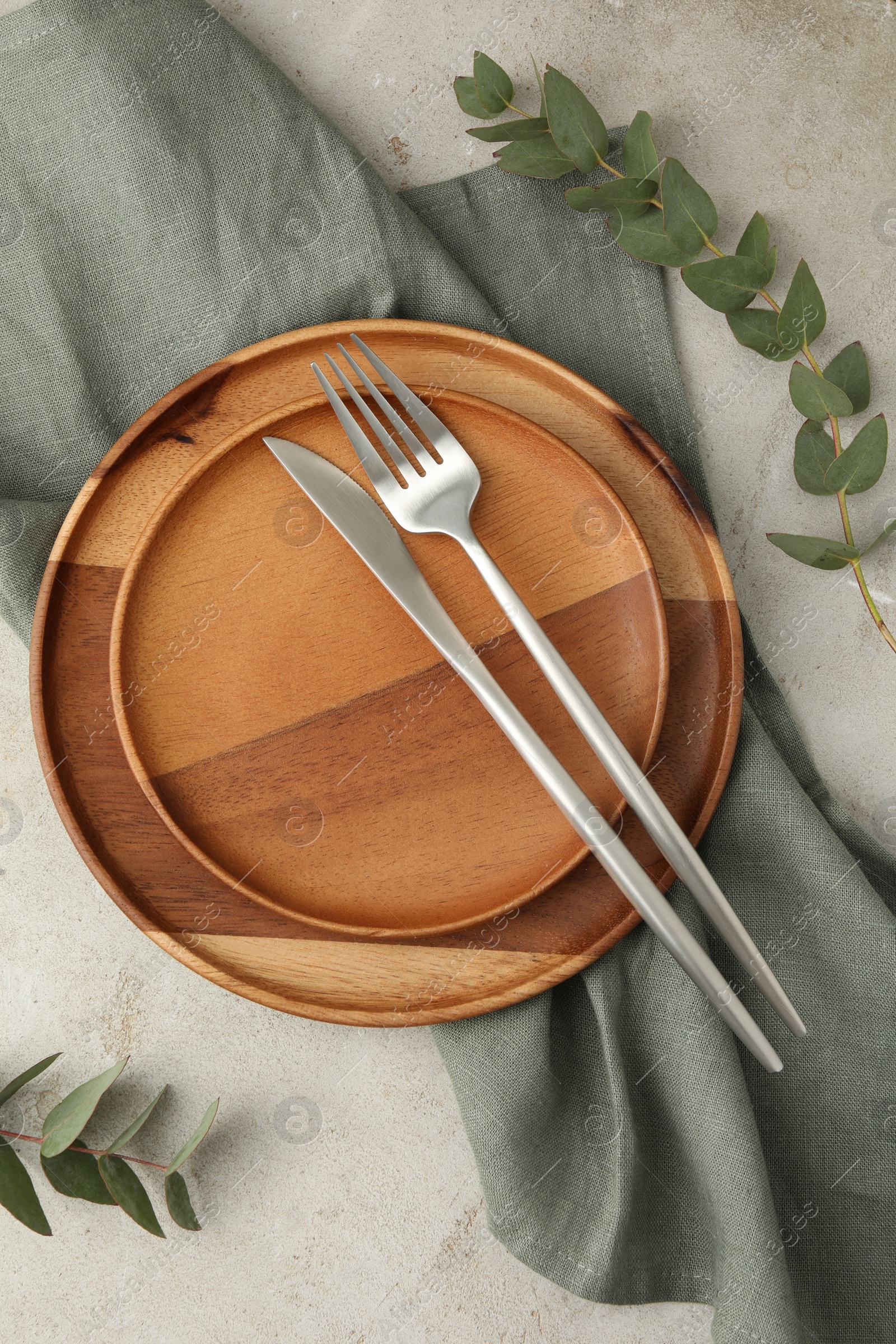 Photo of Stylish setting with cutlery, napkin, eucalyptus branches and plates on light table, flat lay