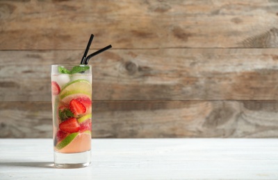 Photo of Glass of refreshing drink with strawberry and lime on table against wooden background. Space for text