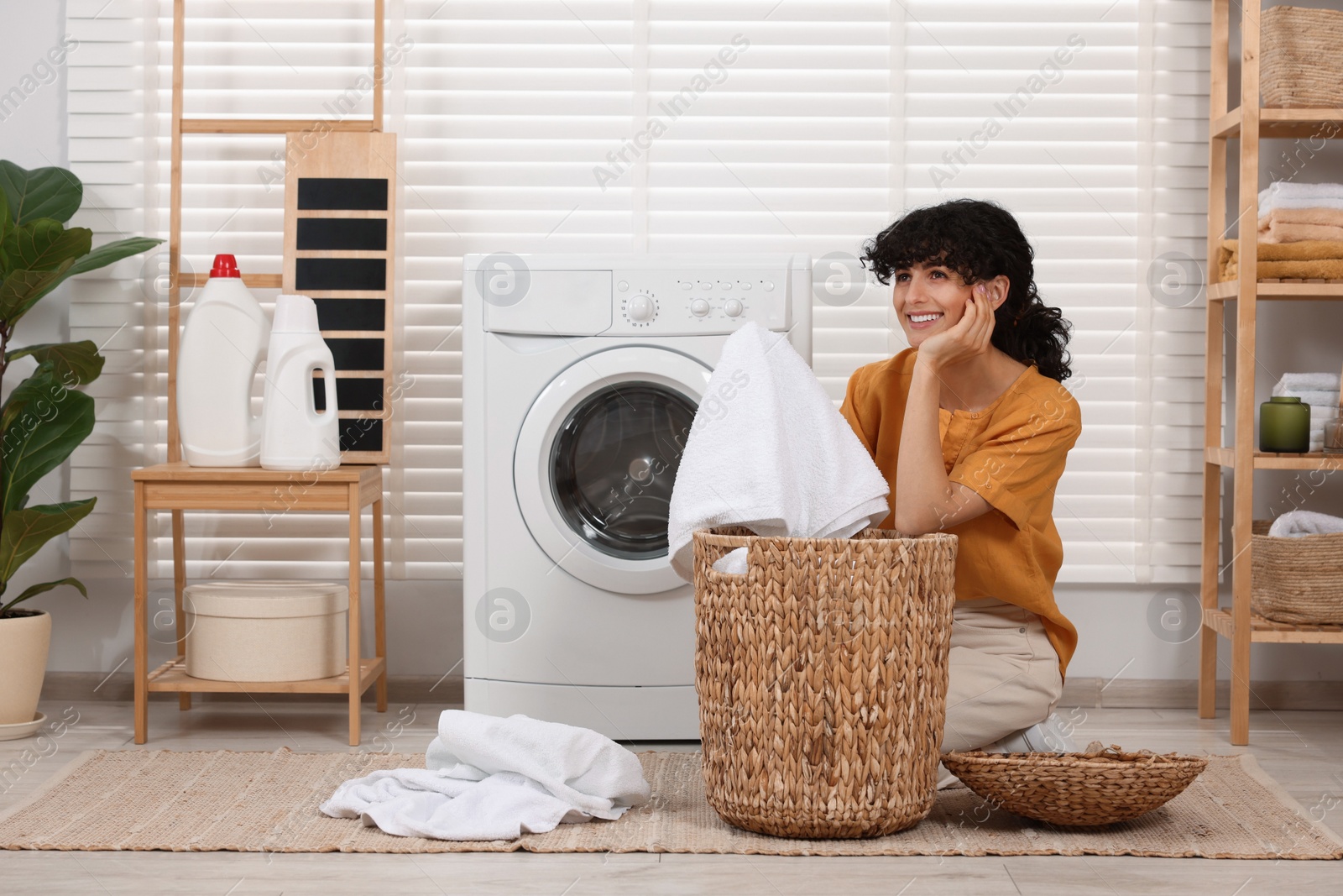 Photo of Happy woman with laundry near washing machine indoors