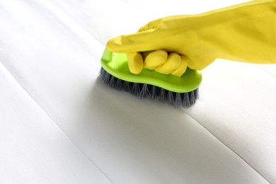 Photo of Woman in yellow gloves cleaning white mattress with brush, closeup. Space for text