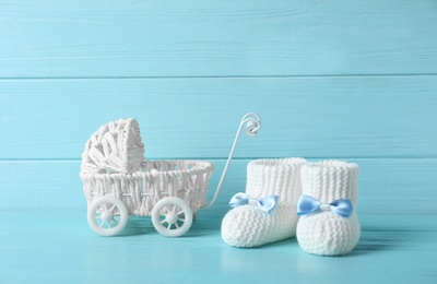 Handmade baby booties and toy buggy on table against wooden background. Space for text