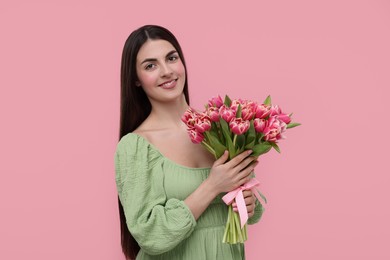 Happy young woman with beautiful bouquet on dusty pink background