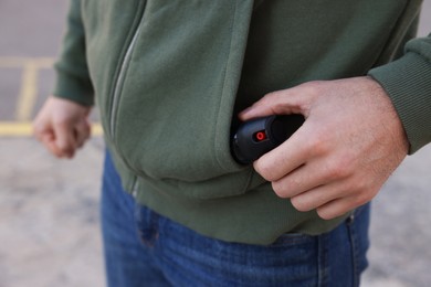 Photo of Man putting pepper spray into sweater pocket outdoors, closeup