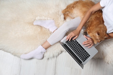 Woman with cute red cat and laptop on fur carpet, top view. Space for text