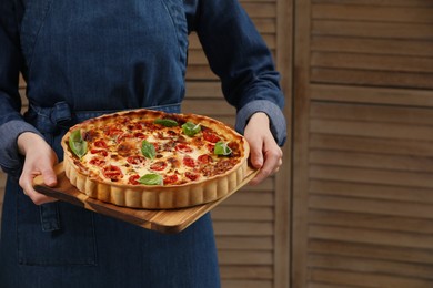 Photo of Woman holding delicious homemade quiche with prosciutto against wooden folding screen, closeup. Space for text