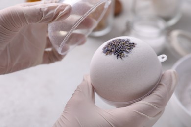 Photo of Woman in gloves with self made bath bomb at table, closeup