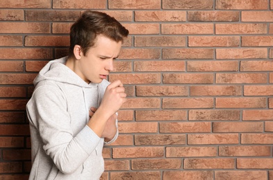 Photo of Teenage boy suffering from cough near brick wall. Space for text