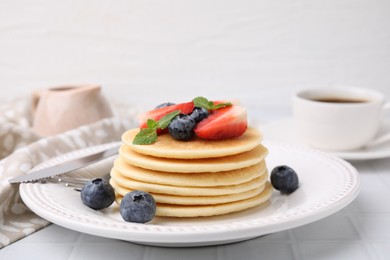 Photo of Delicious pancakes with strawberries, blueberries and mint on white tiled table, closeup