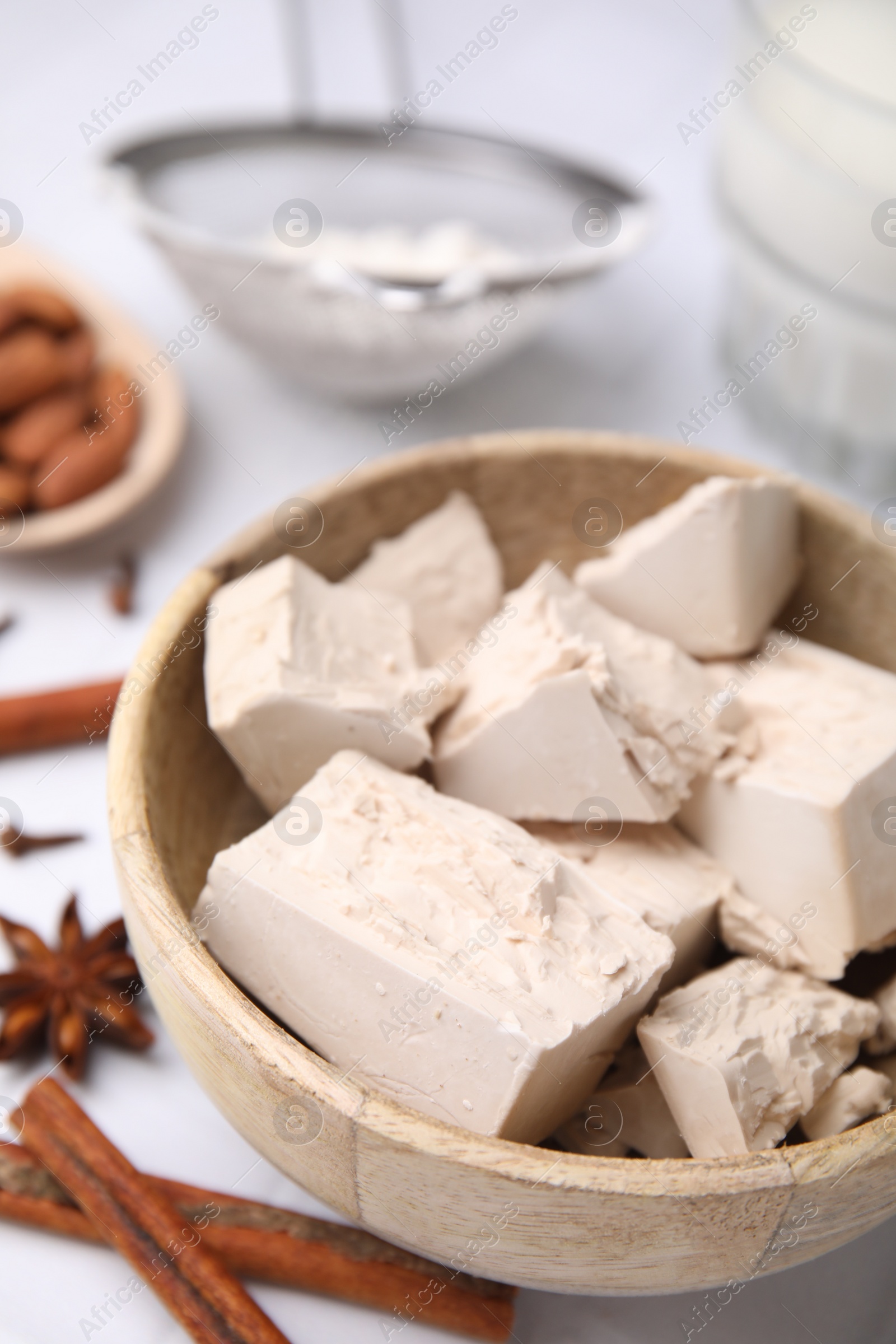 Photo of Wooden bowl with compressed yeast on white table, closeup