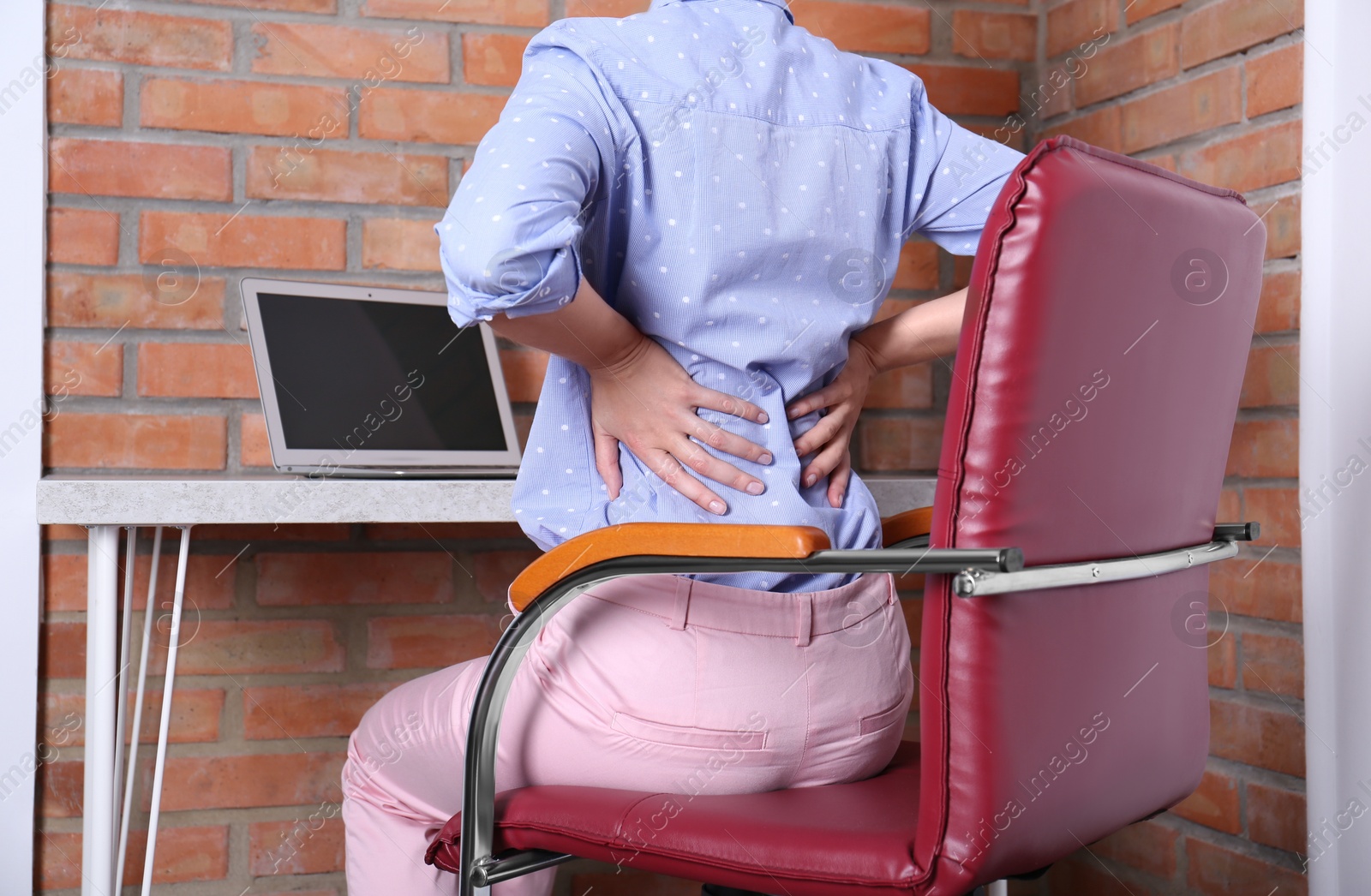 Photo of Woman with lower back pain sitting in office chair at table, closeup