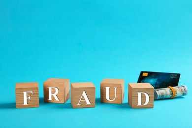 Photo of Wooden cubes with word Fraud, credit card and money on light blue background, space for text