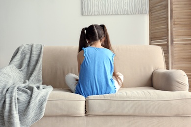 Photo of Lonely little girl sitting on sofa at home. Autism concept
