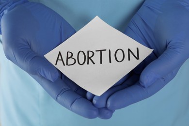 Photo of Doctor holding paper card with word ABORTION, closeup