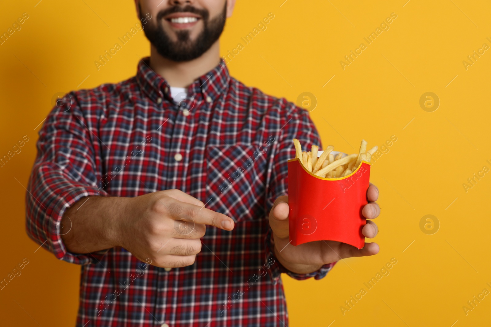 Photo of Young man with French fries on orange background, closeup