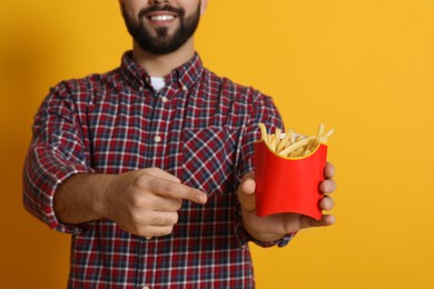 Photo of Young man with French fries on orange background, closeup