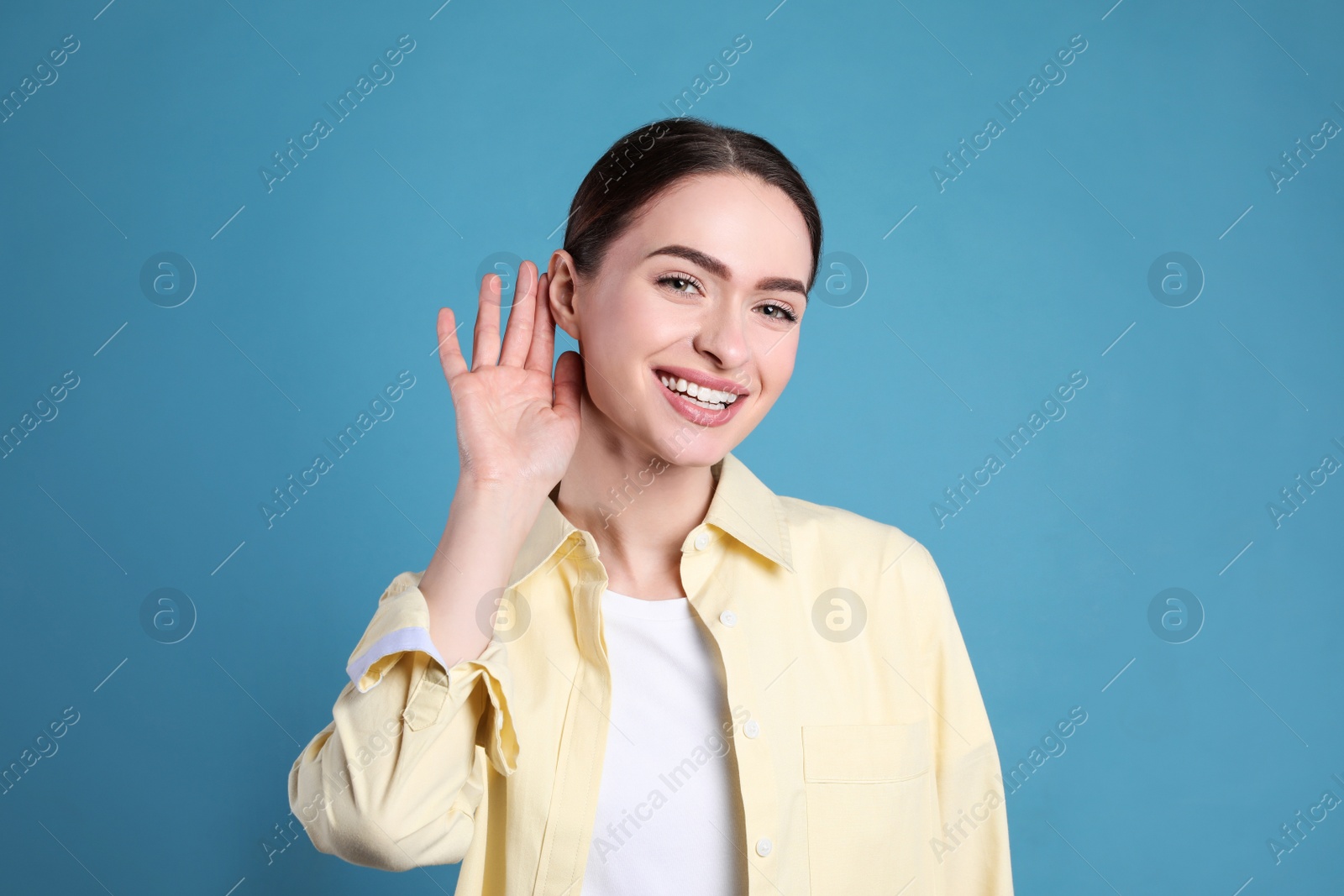 Photo of Young woman showing hand to ear gesture on light blue background