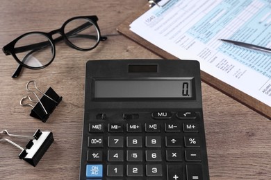 Photo of Tax accounting. Calculator, document, glasses and stationery on wooden table, closeup
