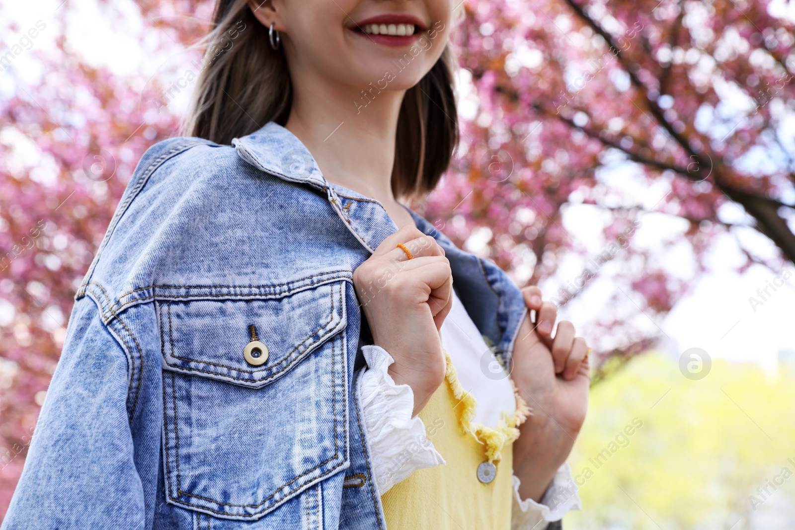 Photo of Beautiful young woman in park with blossoming sakura trees, closeup