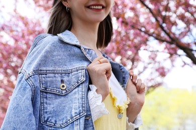 Beautiful young woman in park with blossoming sakura trees, closeup