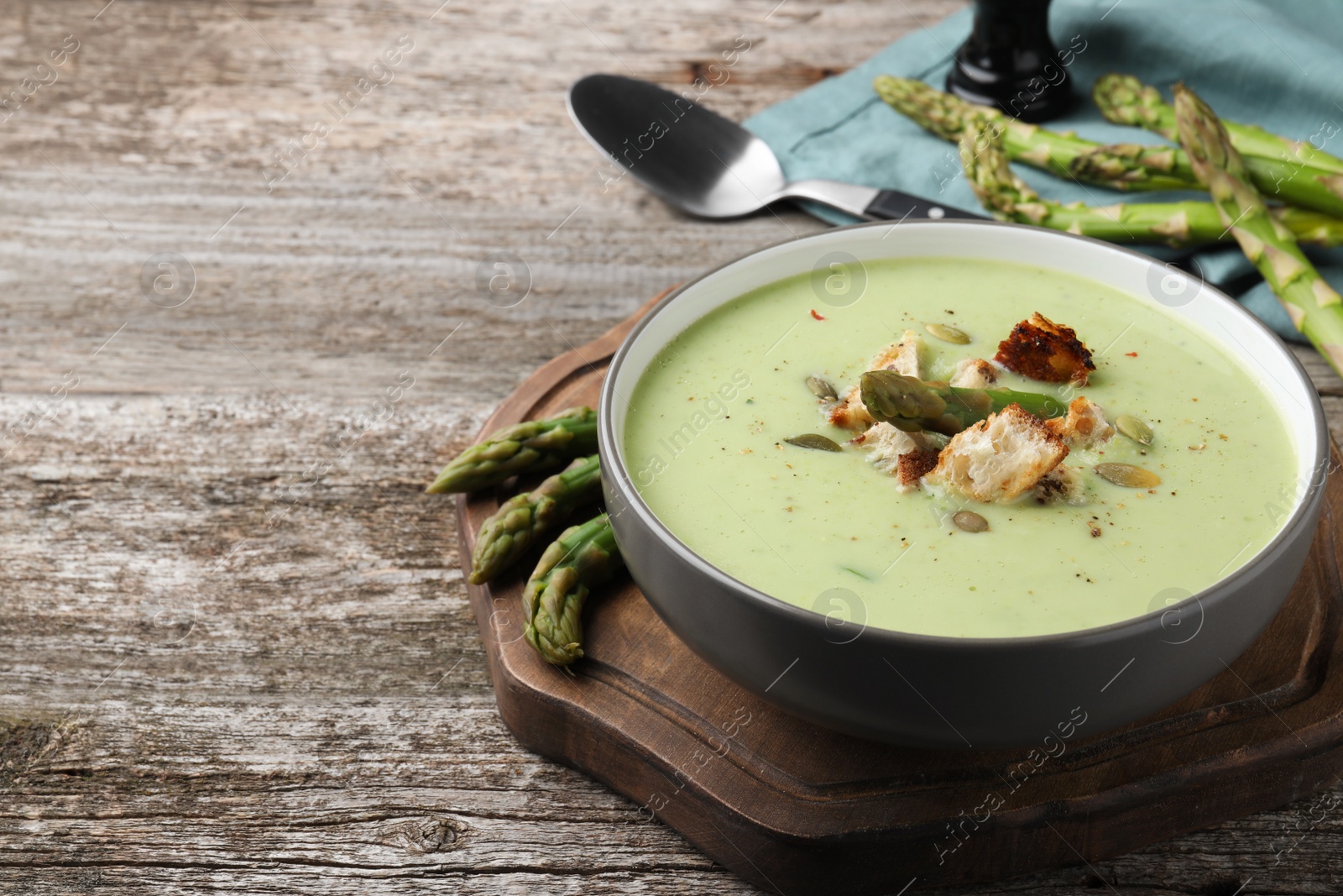 Photo of Bowl of delicious asparagus soup on wooden table, space for text