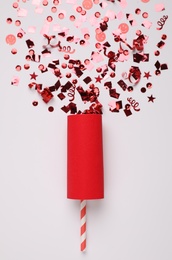 Photo of Shiny red confetti bursting out of party cracker on light background, top view