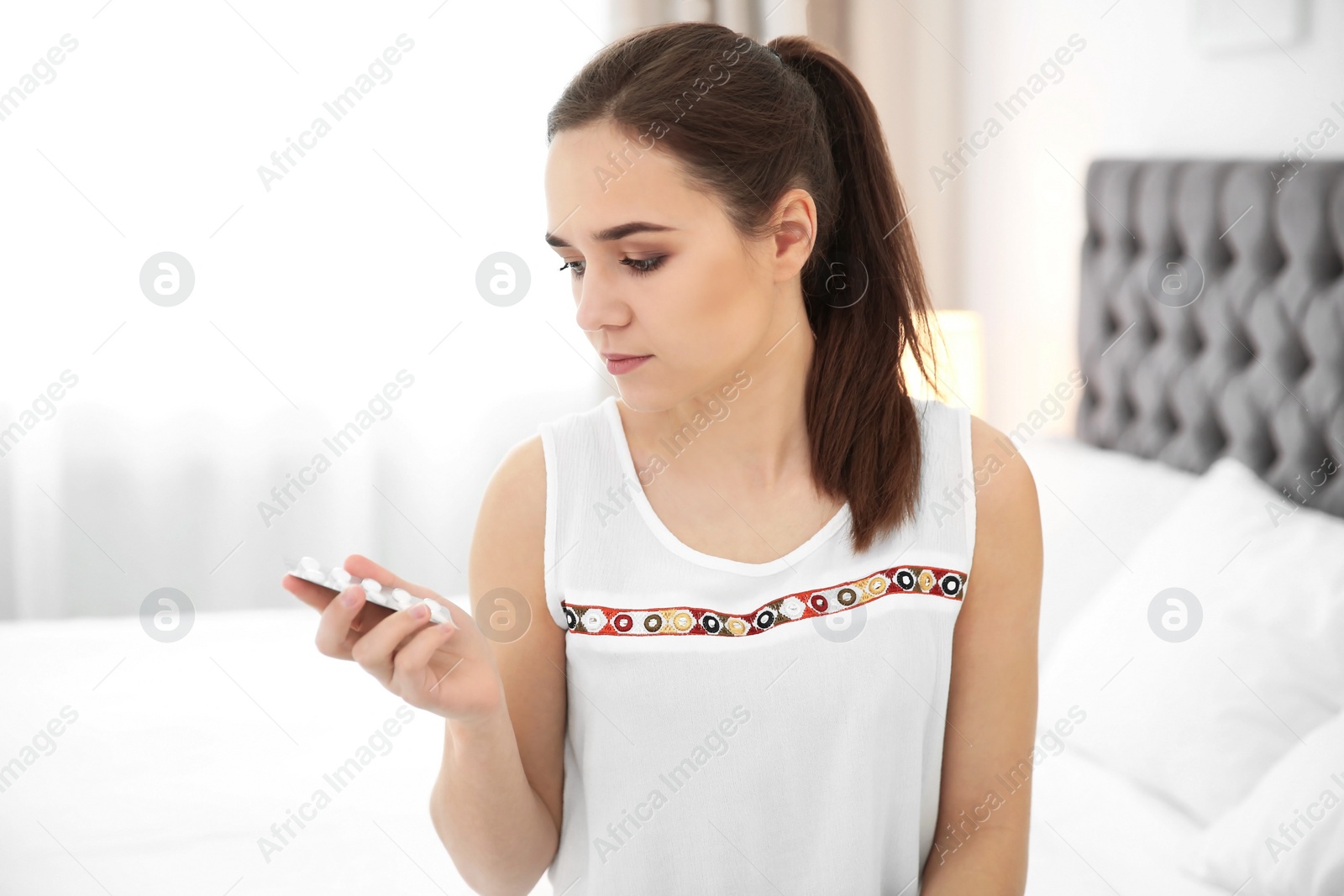 Photo of Young woman holding blister with pills indoors