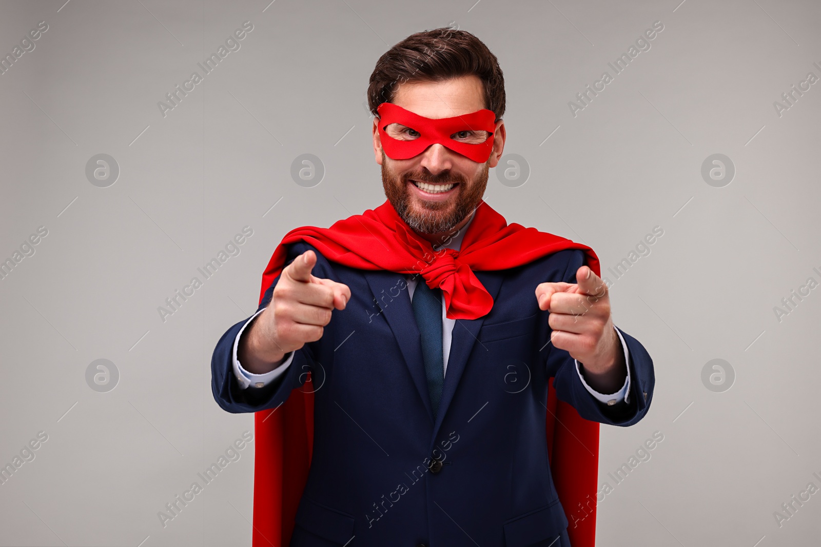 Photo of Happy businessman wearing red superhero cape and mask on beige background