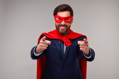 Happy businessman wearing red superhero cape and mask on beige background