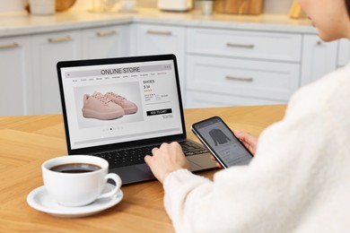 Photo of Woman with laptop and smartphone shopping online at wooden table in kitchen, closeup