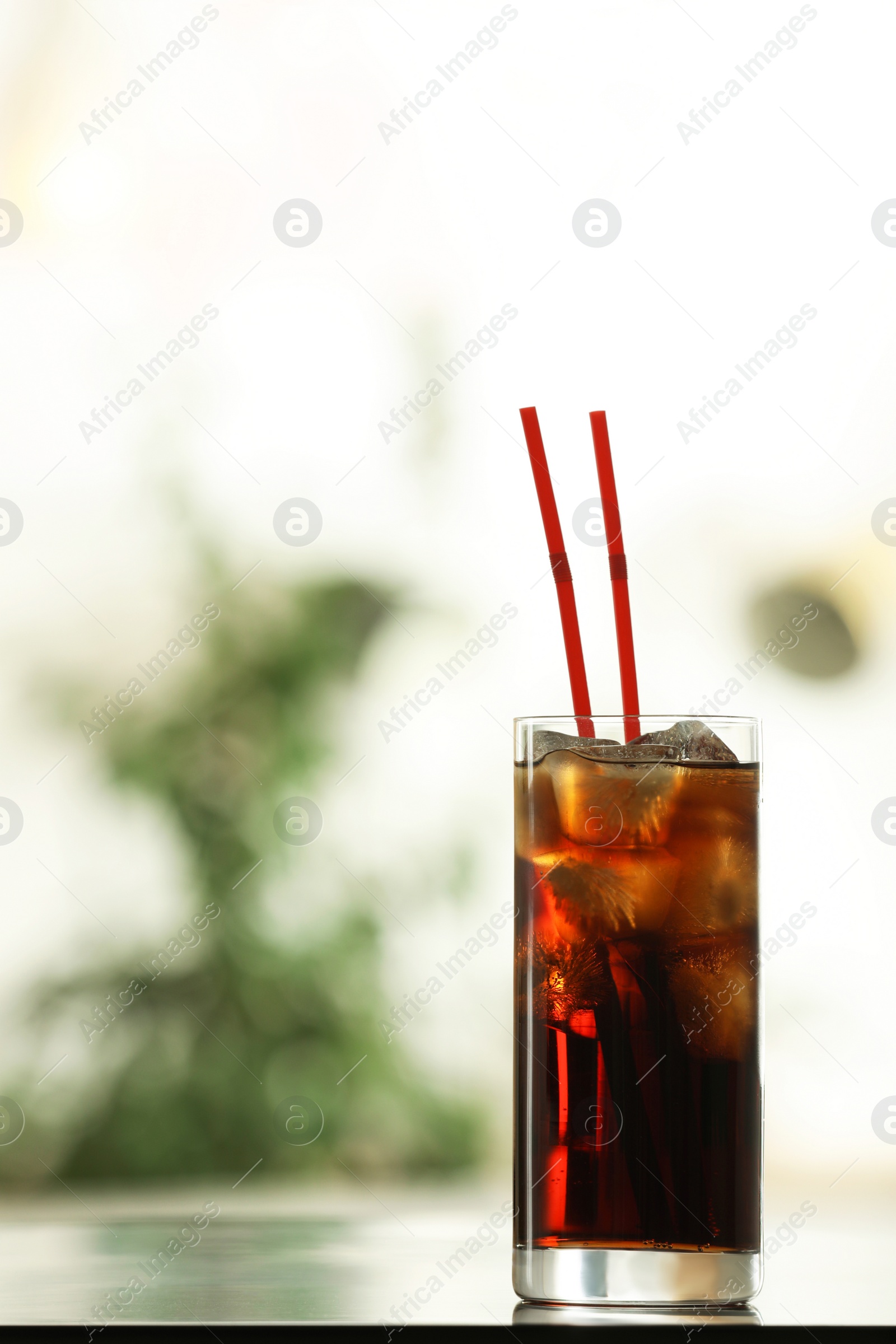 Photo of Glass of cola with ice on table against blurred background. Space for text