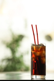 Photo of Glass of cola with ice on table against blurred background. Space for text