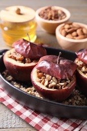 Tasty baked apples with nuts and honey in baking dish on wooden table, closeup