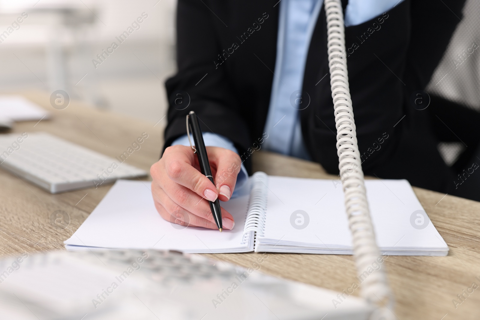 Photo of Secretary talking on telephone and writing at table in office, closeup