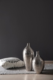 Photo of Beautiful vases and pillow on floor near black wall with space for text. Interior elements