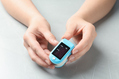 Photo of Woman holding fingertip pulse oximeter at light grey stone table, closeup