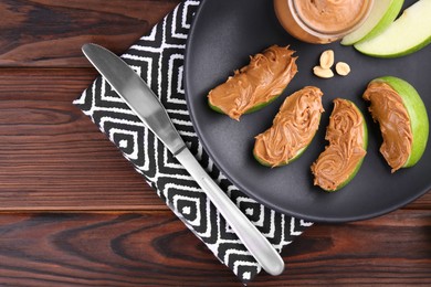 Slices of fresh green apple with peanut butter on wooden table, top view. Space for text