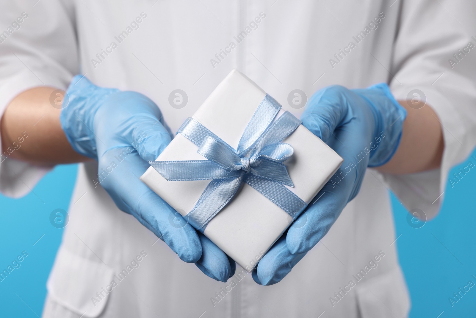 Photo of Doctor holding gift box on light blue background, closeup. Medical present