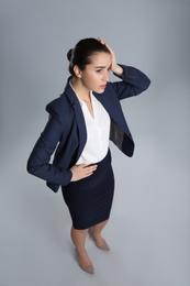 Young stressed businesswoman in elegant suit on grey background