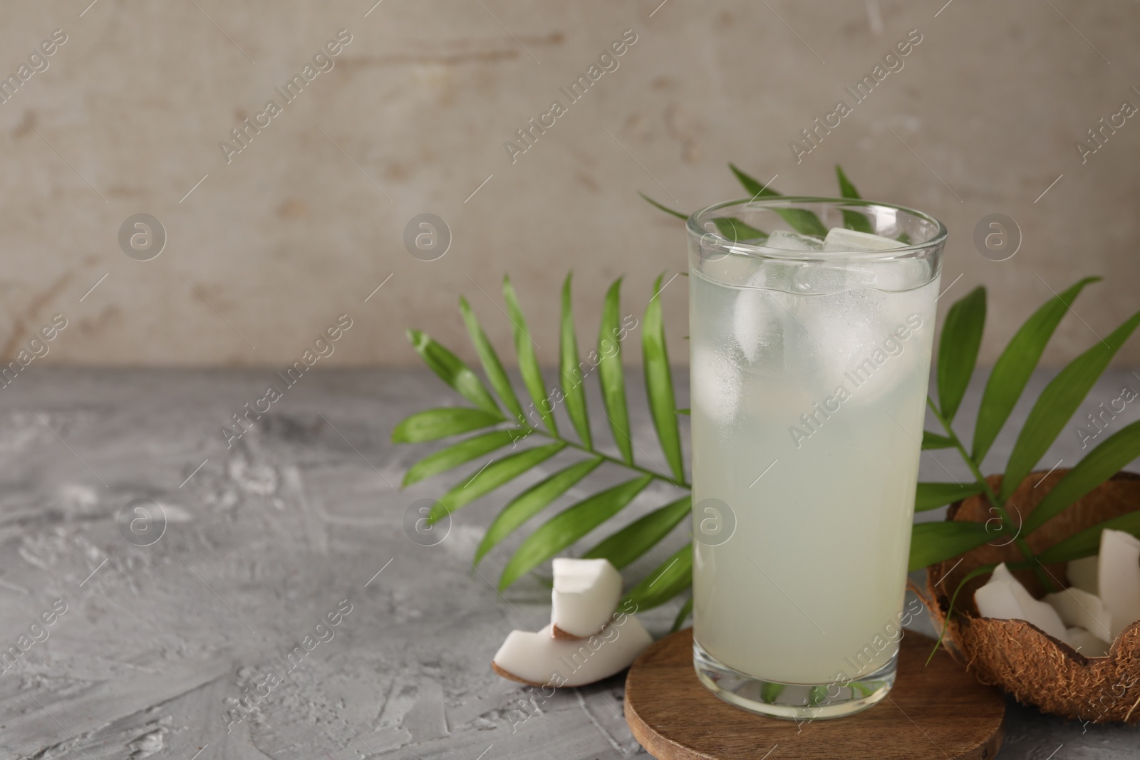 Photo of Glass of coconut water, ice cubes, leaves and nuts on grey table, space for text