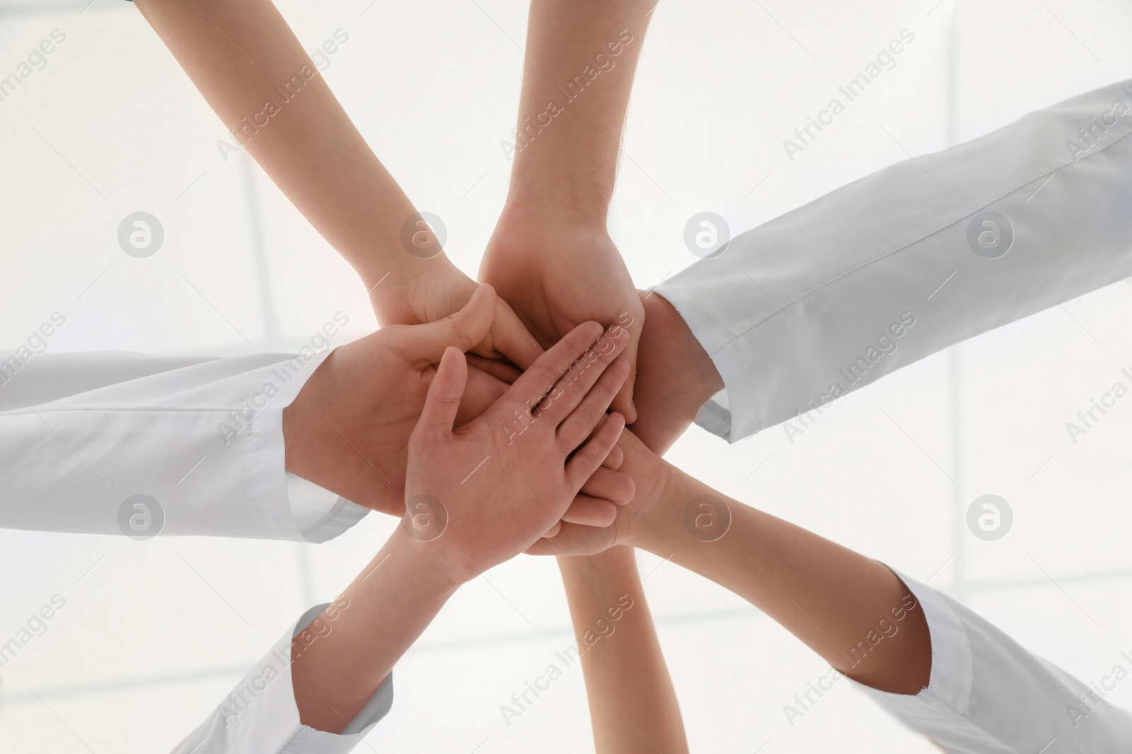 Photo of Team of medical workers holding hands together on light background, bottom view. Unity concept