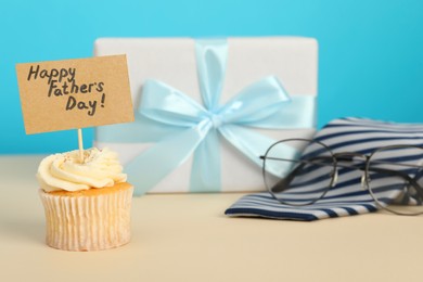 Photo of Happy Father's Day. Tasty cupcake with greetings and presents on beige table, closeup