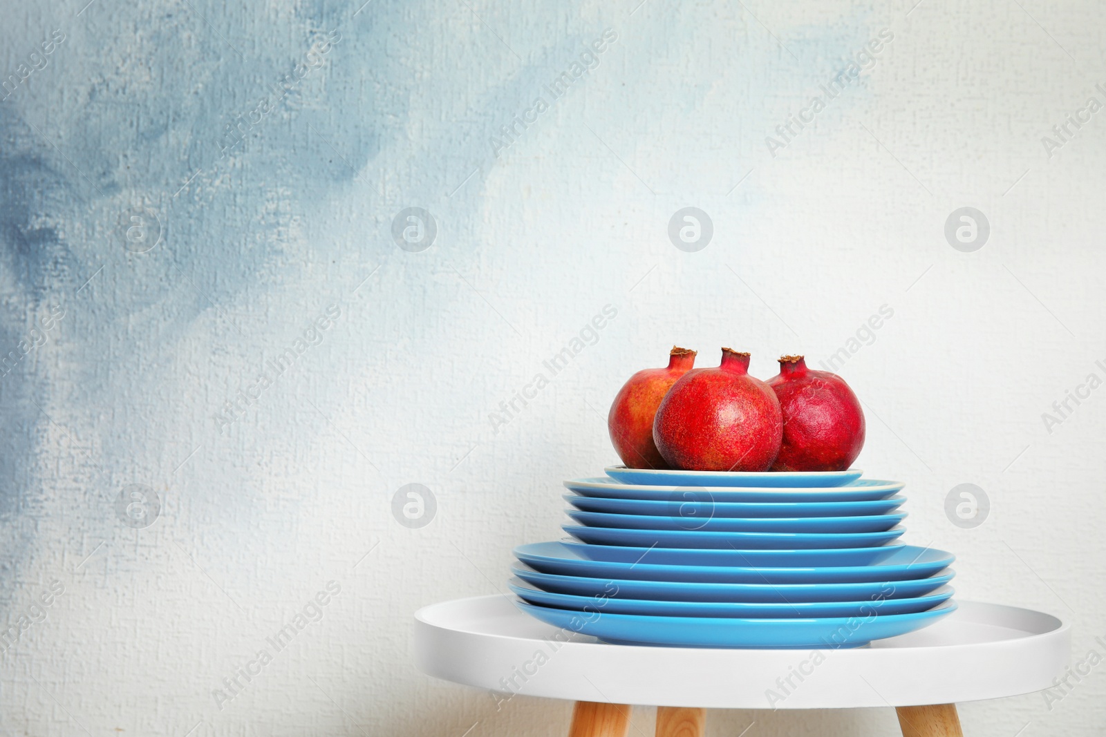 Photo of Stack of plates with pomegranates on table against light background, space for text. Interior element