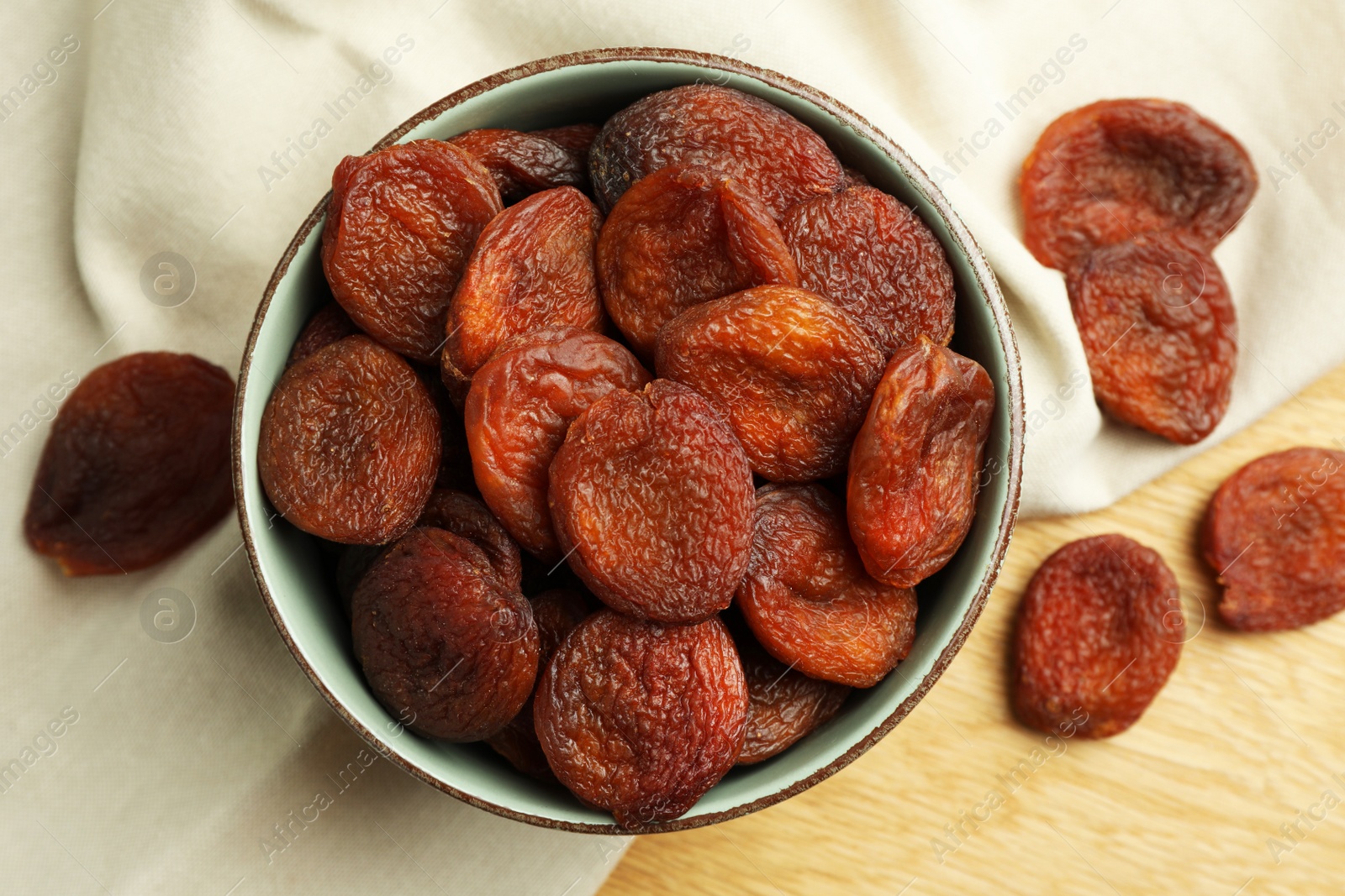 Photo of Tasty apricots with bowl on wooden table, top view. Dried fruits