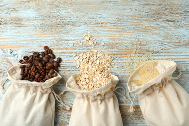 Photo of Cotton eco bags with cereals and coffee beans on wooden table, flat lay