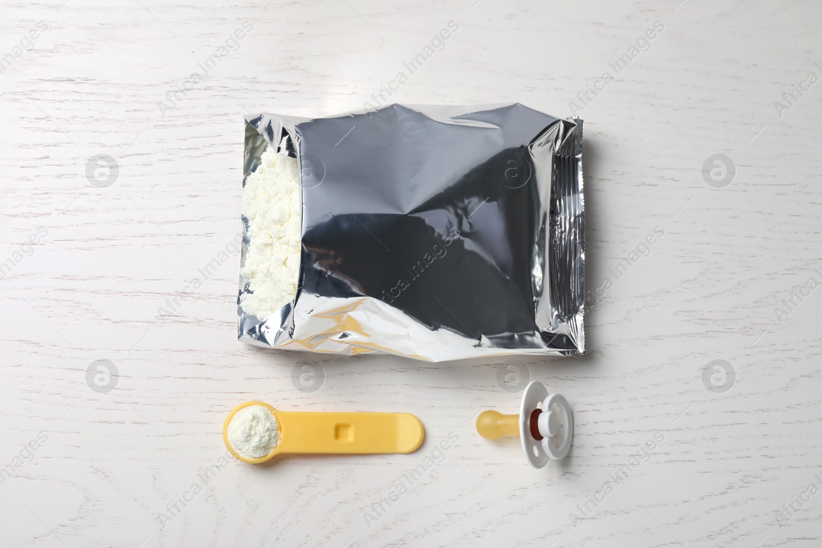 Photo of Bag of powdered infant formula, scoop and pacifier on white wooden table, flat lay. Baby milk